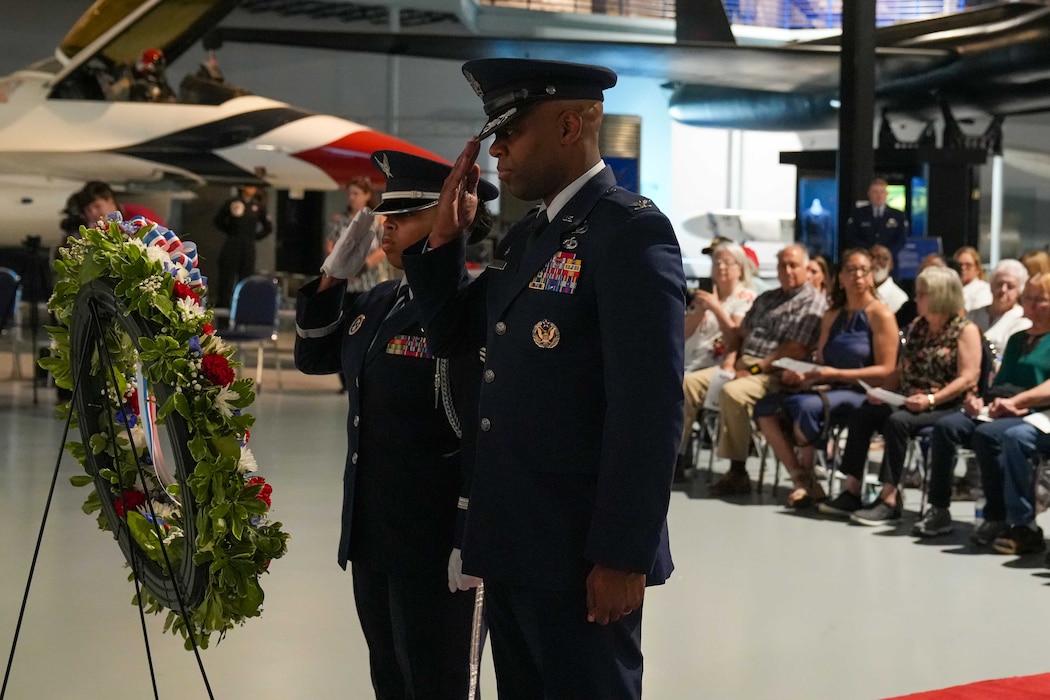 Military personnel salute a memorial wreath