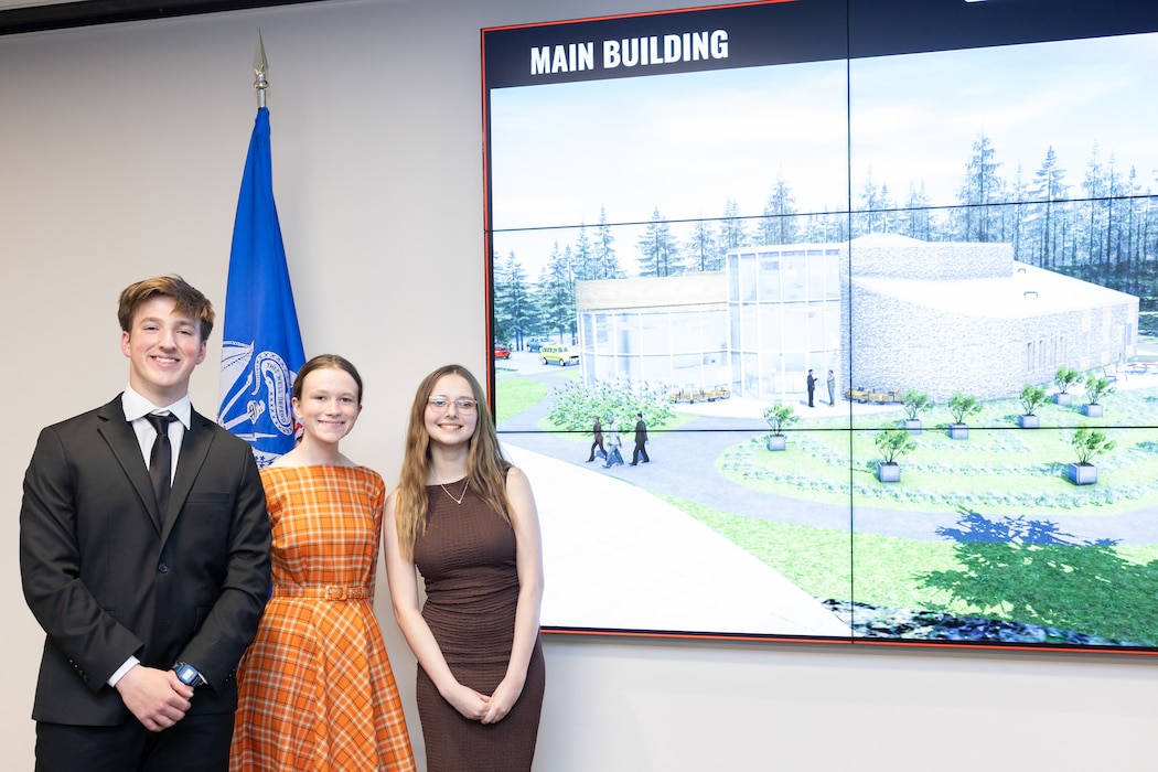 one young man, and two young women standing in front of a monitor with an image of their nature center design.
