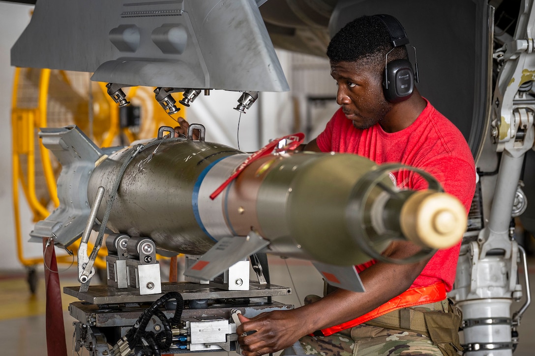 An airman wearing protective earwear works on a laser-guided bomb in a warehouse.