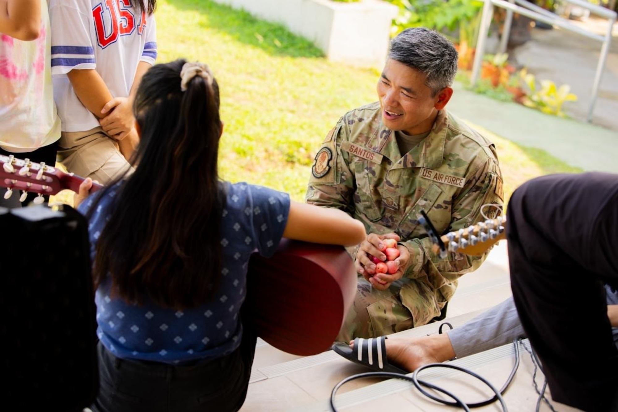 A U.S. soldier smiles at a girl playing guitar in front of him.