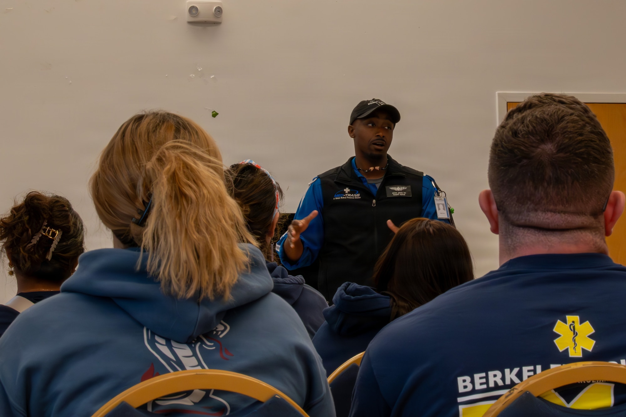 People sit in chairs while a man gives a brief at the front of the room.