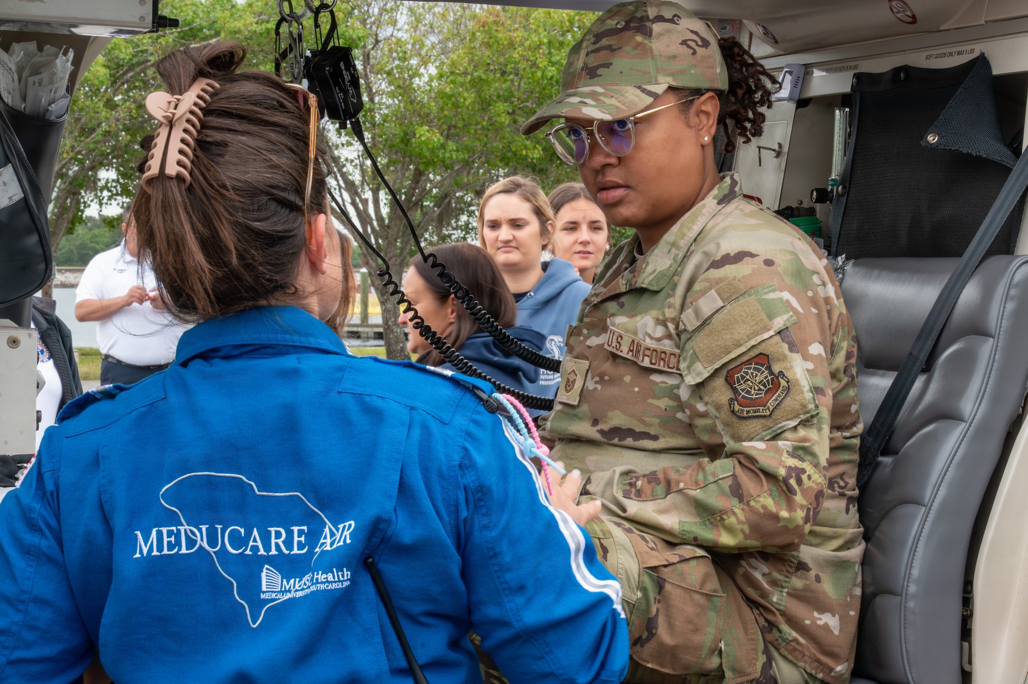 A person in a blue jacket speaks to an Airmen in uniform sitting in a vehicle.