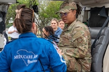 A person in a blue jacket speaks to an Airmen in uniform sitting in a vehicle.