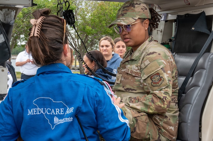 A person in a blue jacket speaks to an Airmen in uniform sitting in a vehicle.
