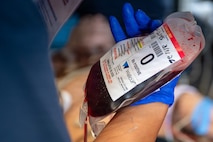 Someone wearing a blue latex glove holds a blood bag.