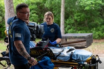 Two people attend to medical equipment standing next to a gurney.