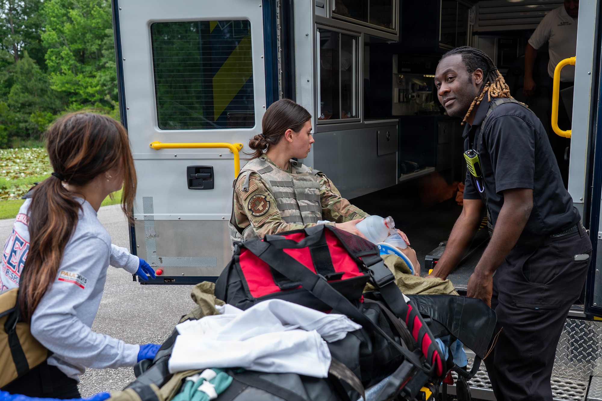 Three people push a gurney with a patient on it into an ambulance.