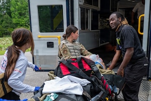 Three people push a gurney with a patient on it into an ambulance.