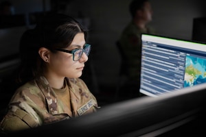 A woman wearing a camouflage military uniform uses a computer in a dark room.
