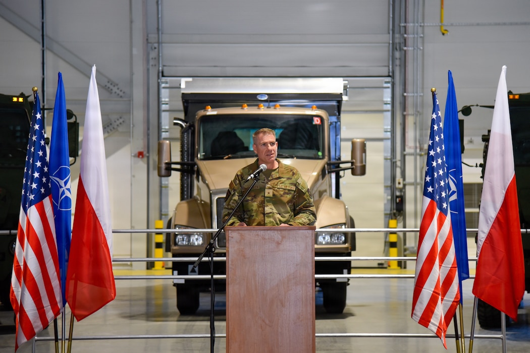 man standing behind podium and in front of large truck