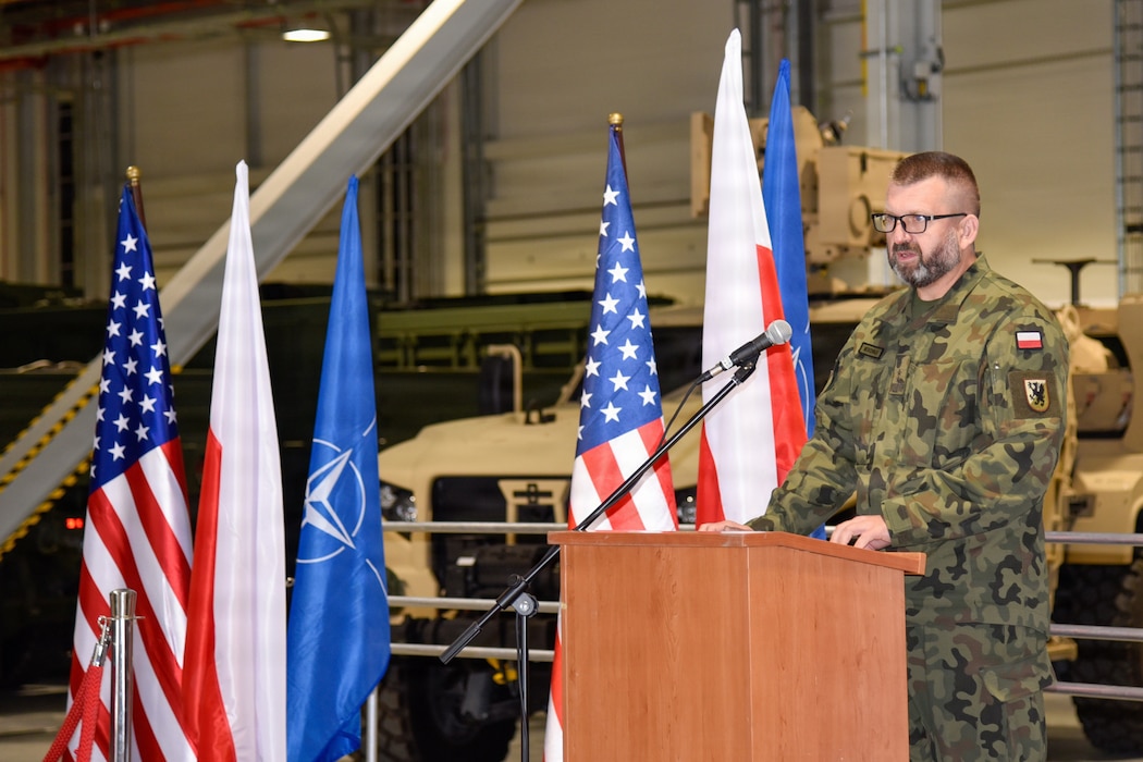 man standing at podium next to a row of flags