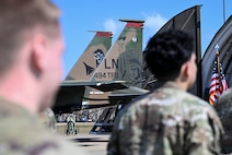 The camo painted F15E Strike Eagle is displayed being framed by two Airmen that worked on the project.