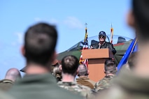 Retired Major stands between Airmen at podium durring a speech.