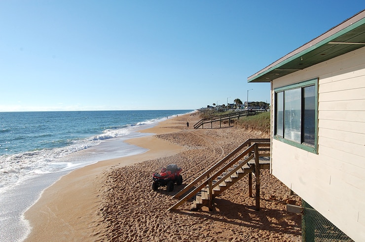 A beachfront of shoreline erosion with a building that has a staircase that leads down to a ATV parked nearby.