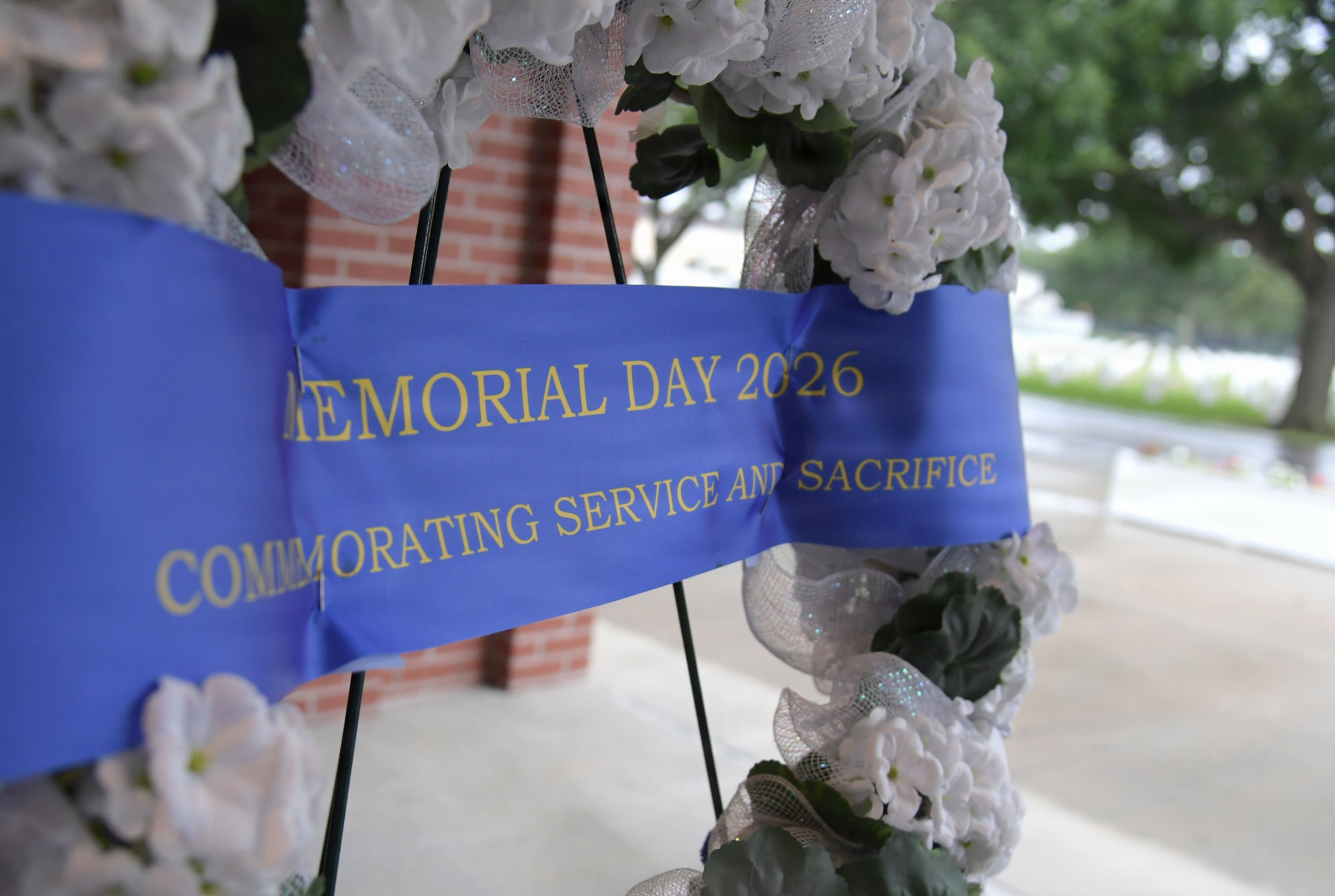A blue Memorial Day ribbon is displayed across a white flowered wreath.