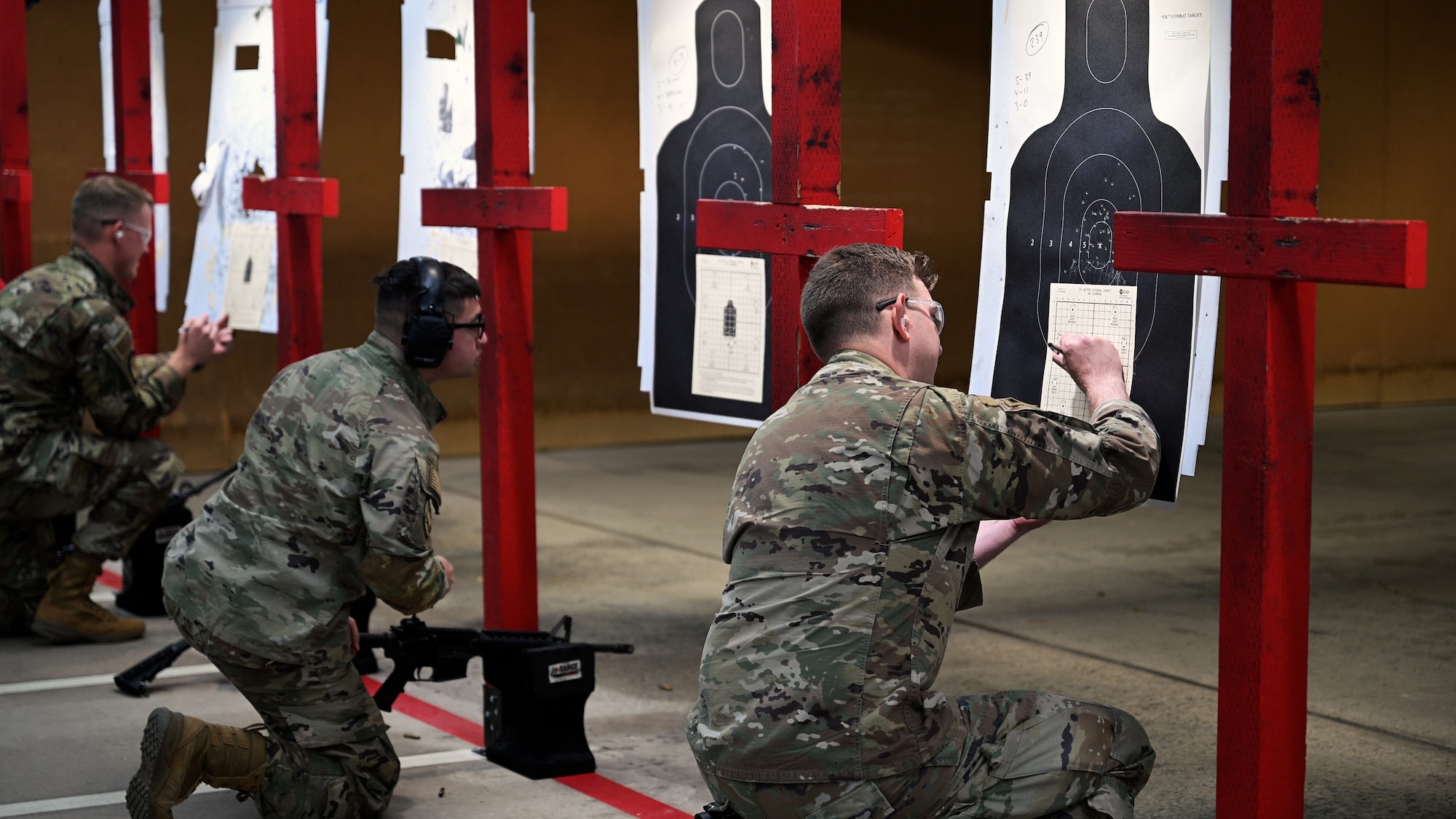 Airmen are kneeling reviewing their targets and recording their scores on a score sheet against the target.