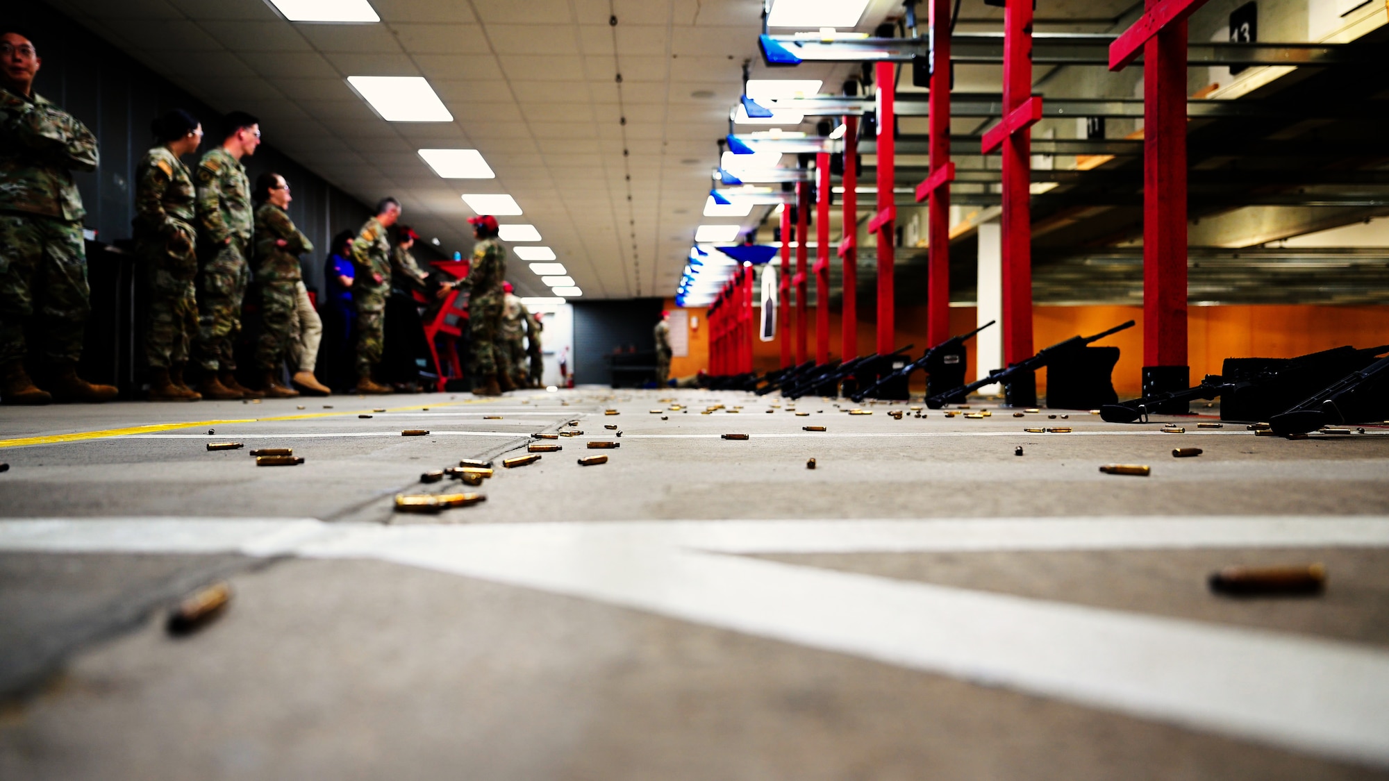 Spent brass casing litter the ground inside the Combat Arms Training and Maintenance range. A line of Airmen are seen on the left side in the background.