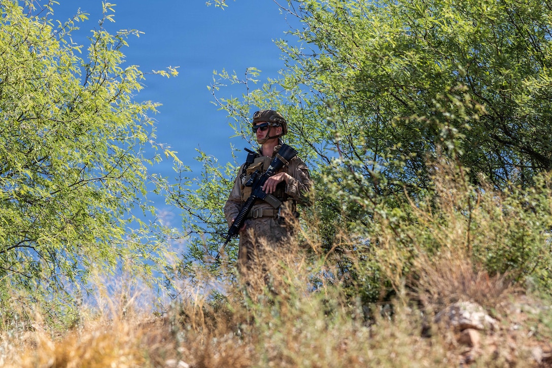 A Marine in camouflage stands outside while holding a machine gun.