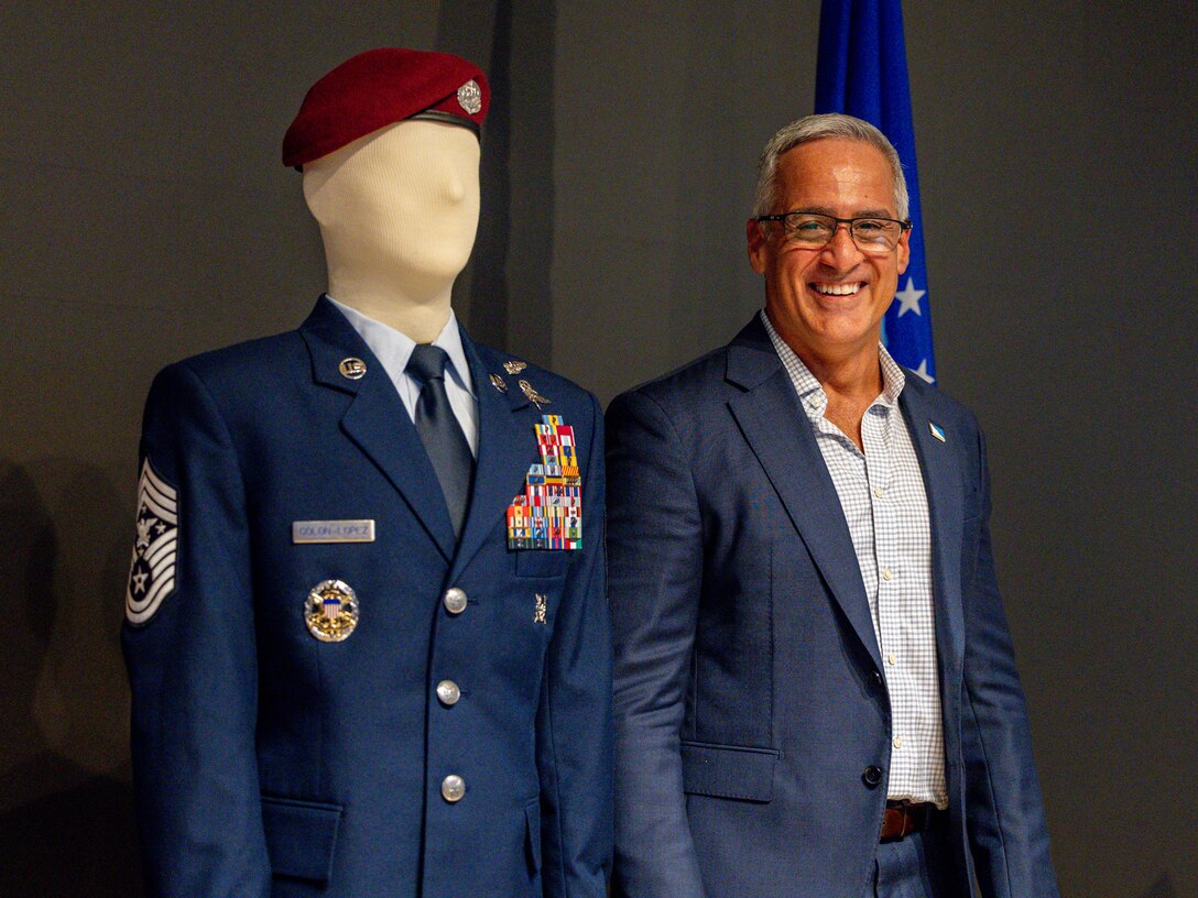 Retired Senior Enlisted Advisor to the Chairman Ramón “CZ” Colón‑López smiles while standing beside a mannequin displaying his service dress during the dedication of the Colón‑López Noncommissioned Officer Academy Auditorium at Sheppard Air Force Base, Texas, May 27, 2026.