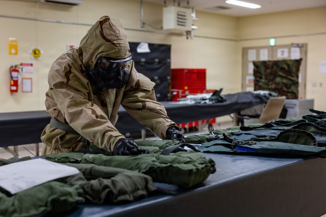U.S. Marine Corps Cpl. Ling Thawng, a flight equipment technician with Marine Aviation Logistics Squadron (MALS) 12, Marine Aircraft Group 12, 1st Marine Aircraft Wing, and a native of Florida, assembles life preservers while wearing Chemical Biological Radiological Nuclear Mission-Oriented Protective Posture gear during a hazardous CBRN drill at Marine Corps Air Station Iwakuni, Japan, May 18, 2026. MALS-12 conducted CBRN training to instill confidence in Marines completing daily operations while in MOPP gear. (U.S. Marine Corps photo by Cpl. Dahkareo Pritchett)