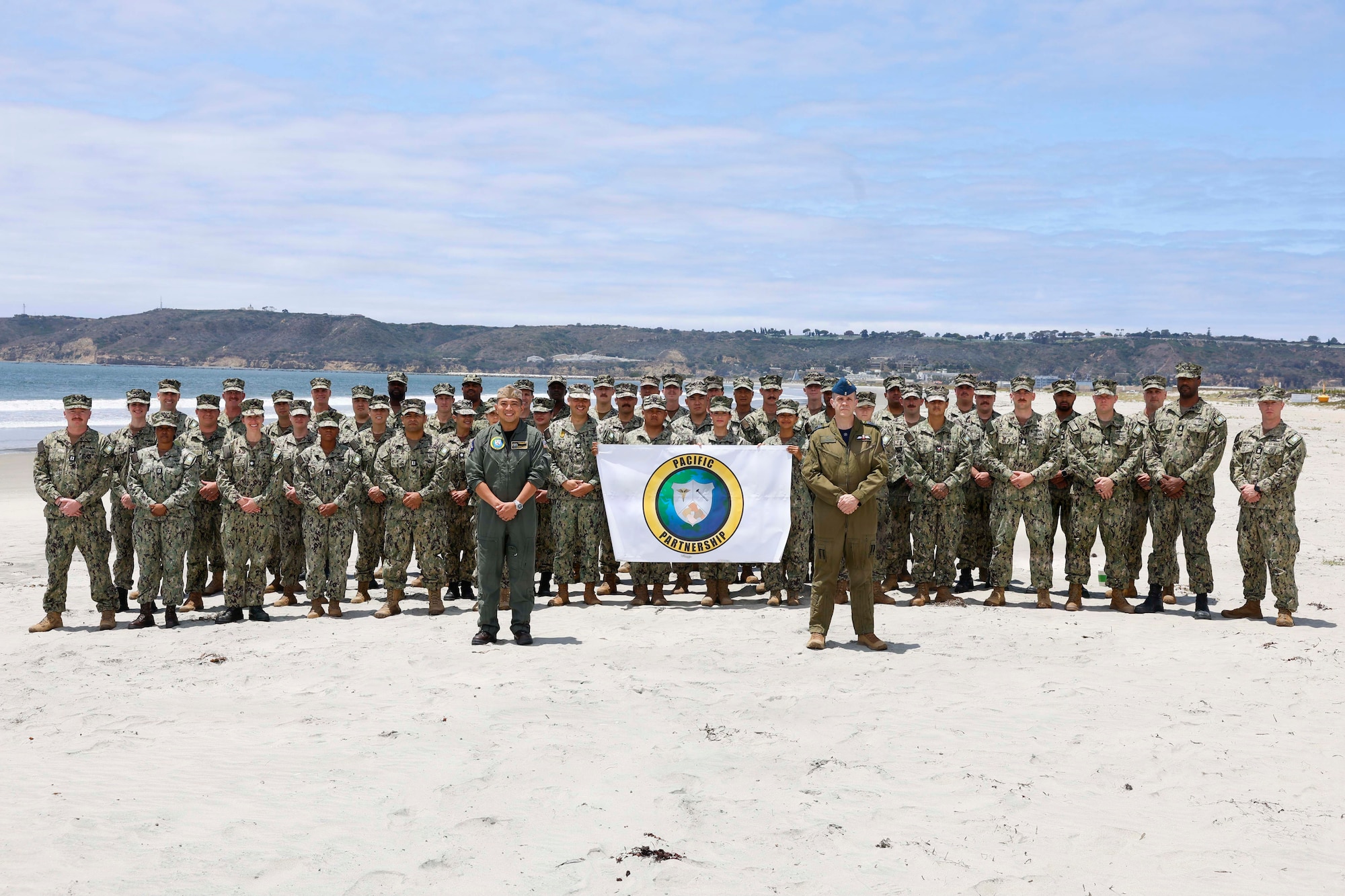NAVAL AIR STATION NORTH ISLAND, Calif. (May 26, 2026) – U.S. Navy Capt. Robert Reyes (left), mission commander of Pacific Partnership 2026 (PP26), Royal Canadian Armed Forces Col. Alain Lafrenière (right), deputy mission commander of PP26, and Sailors pose for a photo commemorating the start of the mission on Naval Air Station North Island, May 26. Now in its 22nd iteration, the Pacific Partnership series is the largest annual multinational humanitarian assistance and disaster management preparedness mission conducted in the Indo-Pacific. Pacific Partnership works collaboratively with host and partner nations to enhance regional interoperability and disaster response capabilities, increase security and stability in the region, and foster new and enduring friendships in the Indo-Pacific. (U.S. Navy Photo by Mass Communication Specialist 1st Class Justin E. Yarborough)
