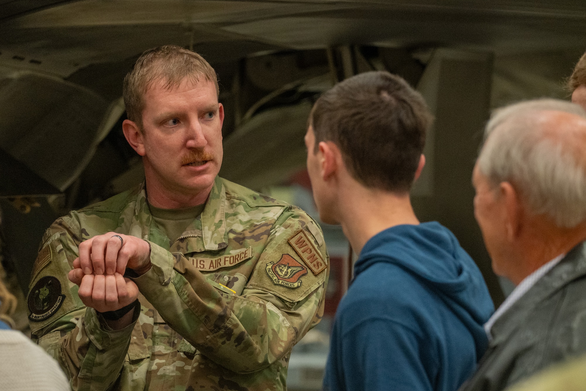 A U.S. Air Force weapons lead crew chief assigned to the 3rd Aircraft Maintenance Squadron, outlines the mechanical process of loading missiles into the internal weapons bay of an F-22 Raptor at Joint Base Elmendorf-Richardson, Alaska, May 21, 2026. Whittaker demonstrated the internal carriage system, which allows the aircraft to maintain its stealth profile while carrying precision-guided munitions. This joint-base event brought together Army and Air Force personnel to offer support, fellowship and technical insight to families of fallen service members. (U.S. Air Force photo by Airman 1st Class Theodore Gowdy)