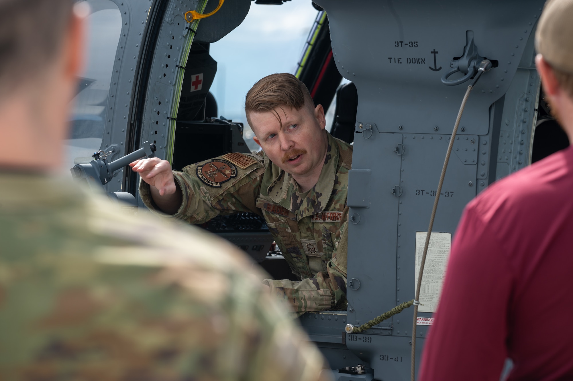 U.S. Air Force Master Sgt. Garrett Bader, the propulsion superintendent assigned to the 176th Maintenance Squadron, demonstrates the operation of an HH-60G Pave Hawk helicopter gunner door during a base tour at Joint Base Elmendorf-Richardson, Alaska, May 21, 2026. The demonstration highlighted the defensive configurations and quick-access capabilities built into the airframe for rescue crews in hostile environments. This joint-base event brought together Army and Air Force personnel to offer support, fellowship and technical insight to families of fallen service members. (U.S. Air Force photo by Airman 1st Class Theodore Gowdy)