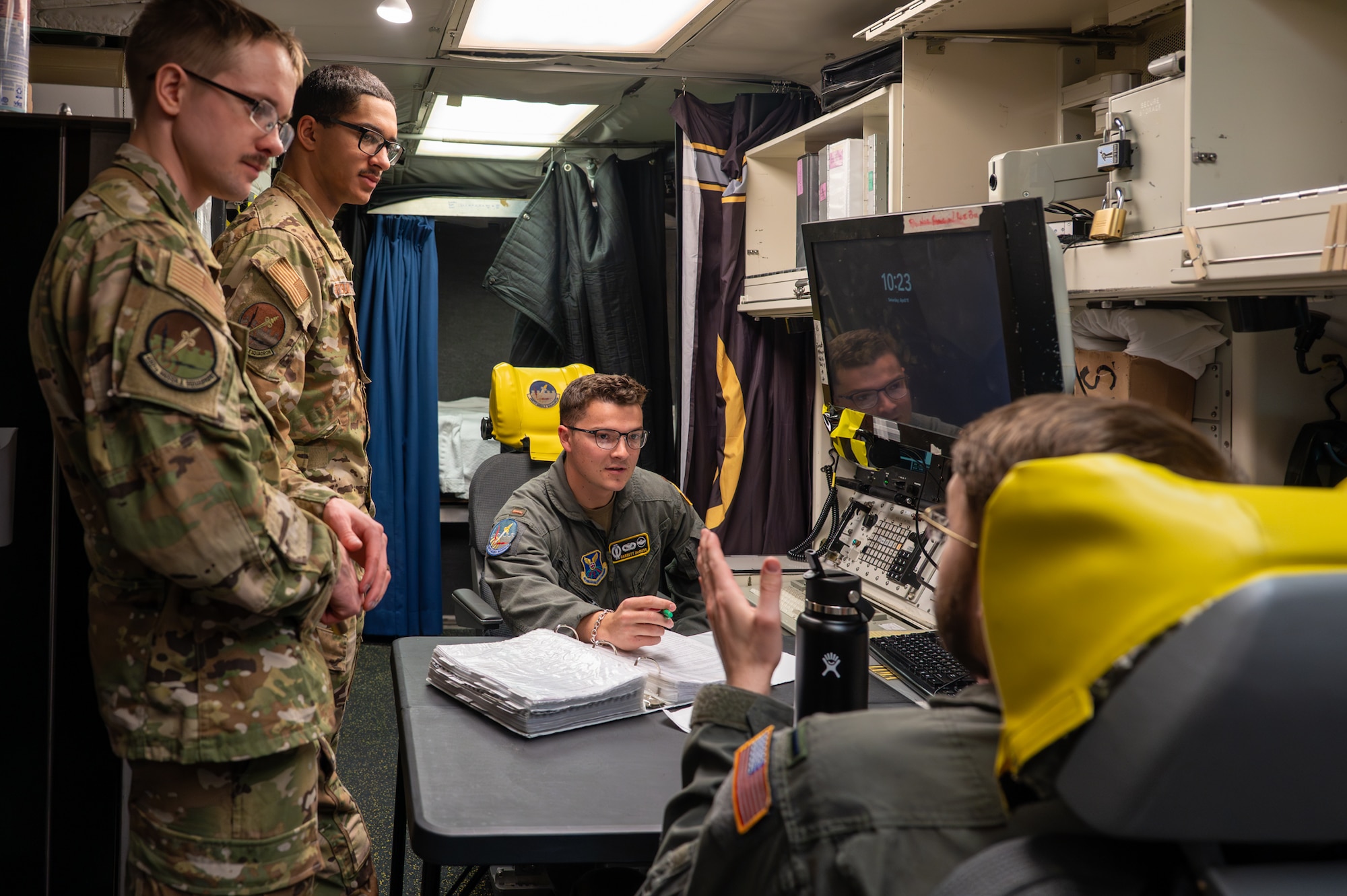 A group of uniformed personnel talks in a launch control center.