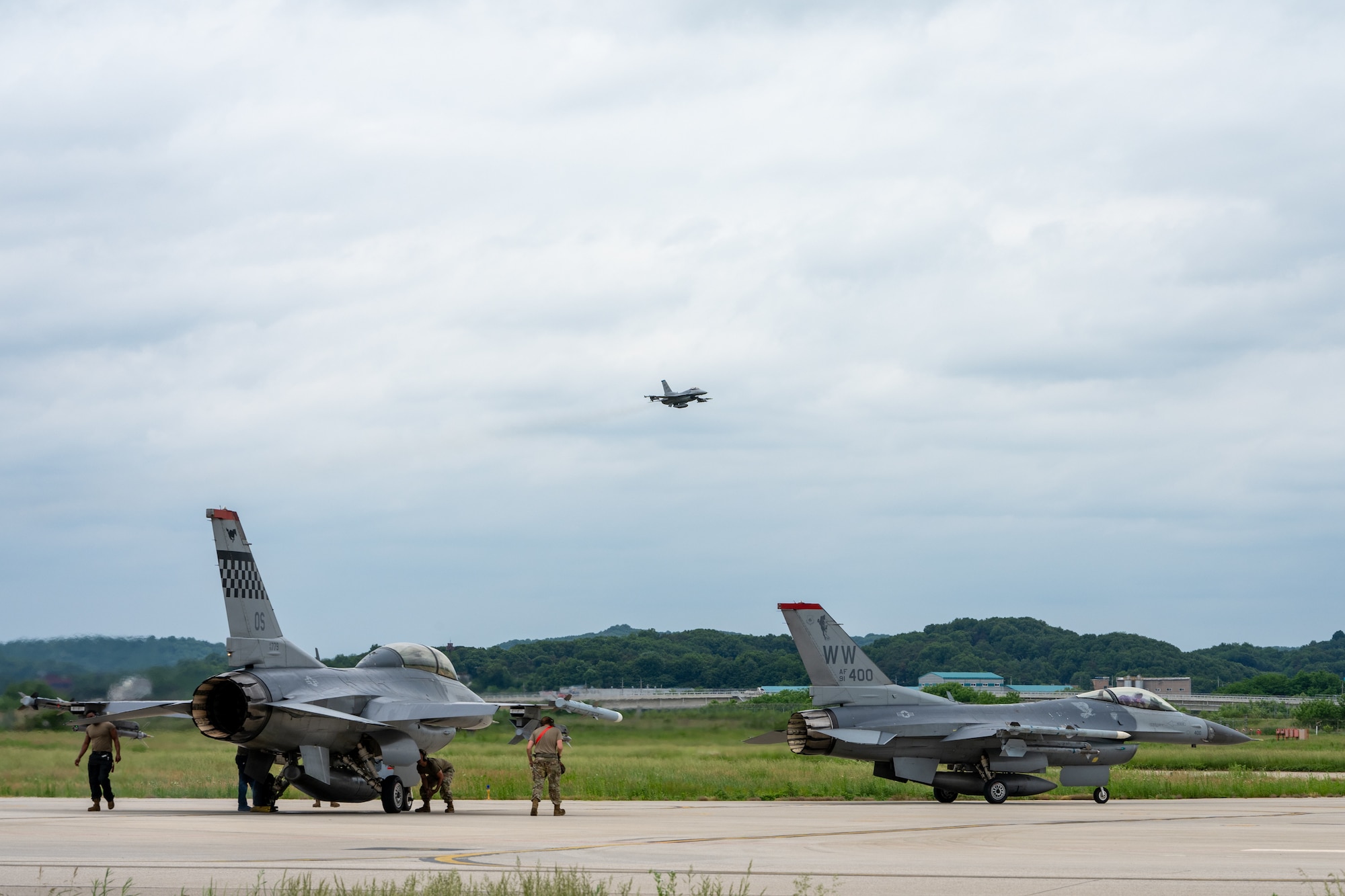 An aircraft flies low over the runway as two aircraft taxi to park.