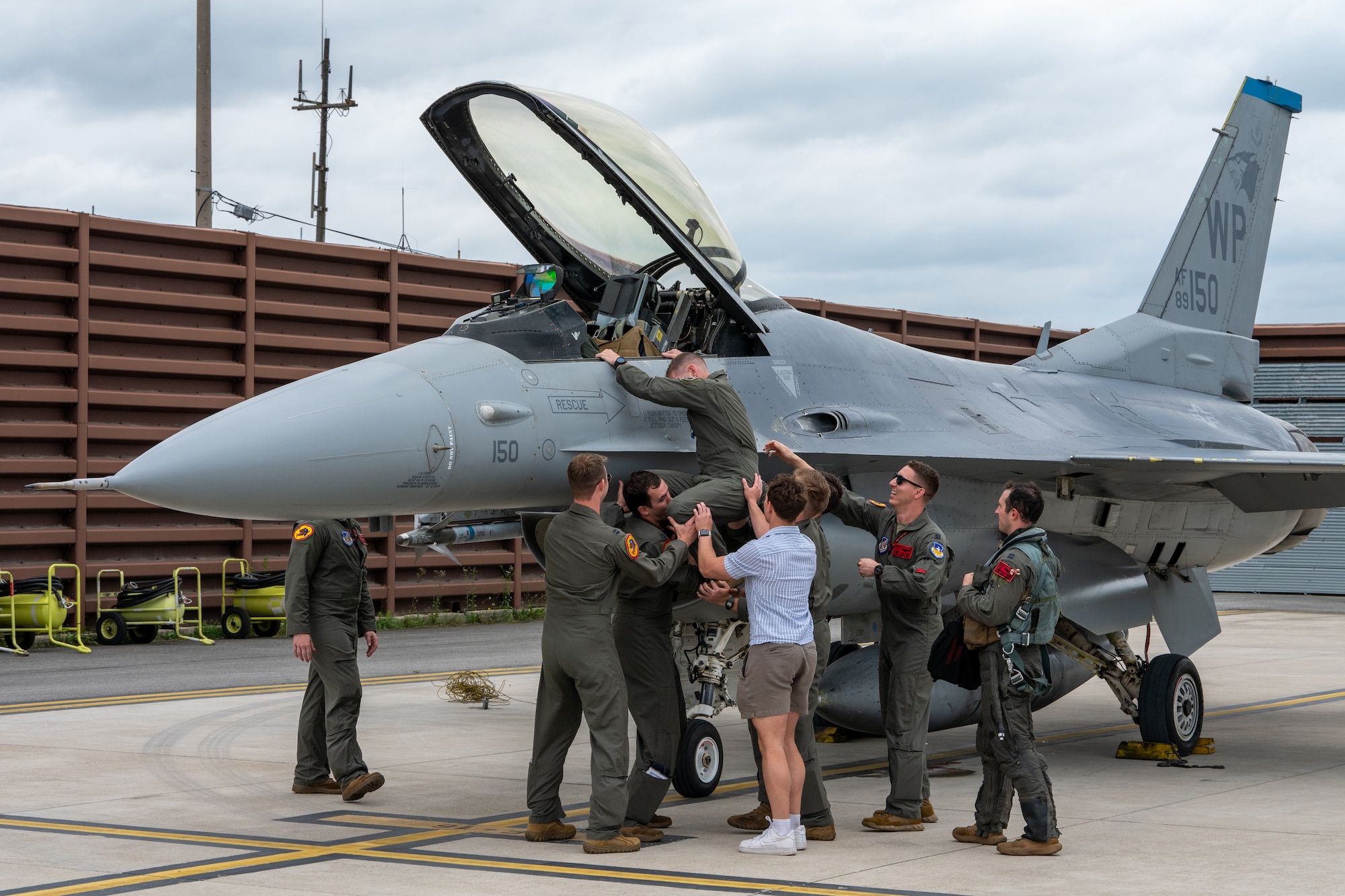 Pilots assist another pilot from the cockpit of a fighter jet.