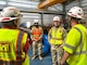 Two men in Army uniforms talk to two men in safety vests and hardhats inside of a power plant