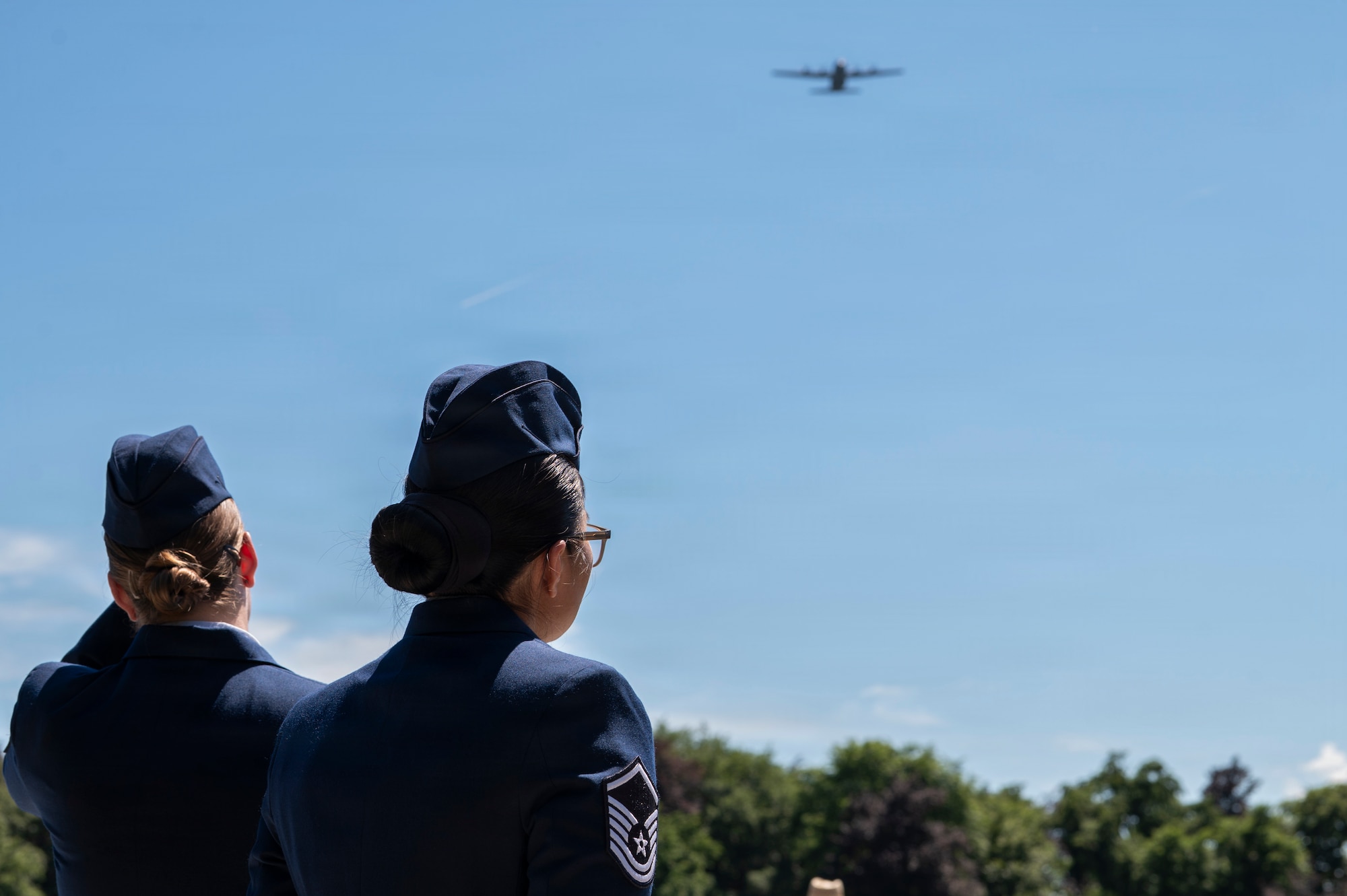 A photo of two Airman watching an aircraft fly overhead during a Memorial Day ceremony at Luxembourg American Cemetery.
