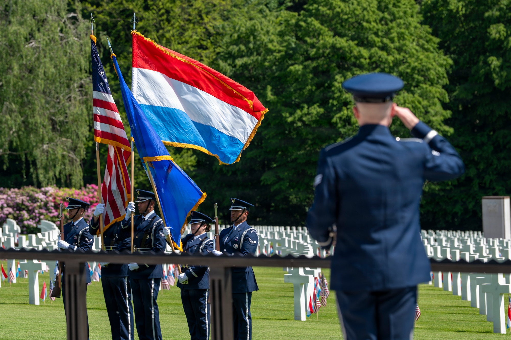 A photo of an Airman saluting the U.S. flag held by Ramstein Air Base Honor Guardsmen during a Memorial Day ceremony at Luxembourg American Cemetery.
