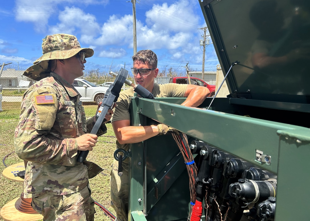 Two men in Army uniforms work on a equipment that supports electricity generation