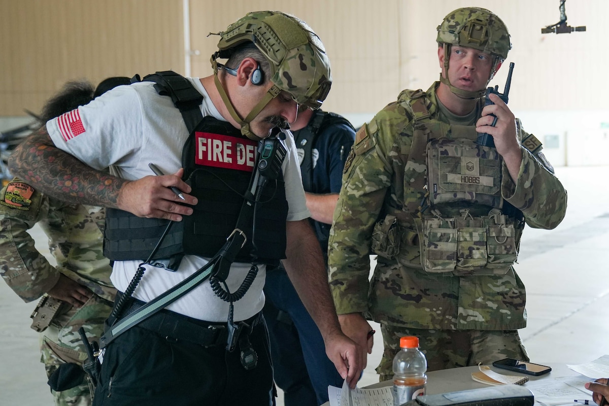 a fire station chief reads documents alongside a security forces airman who is talking on a radio