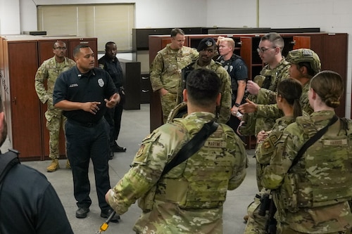 a police officer is surrounded by Airmen in uniform as he speaks to the group