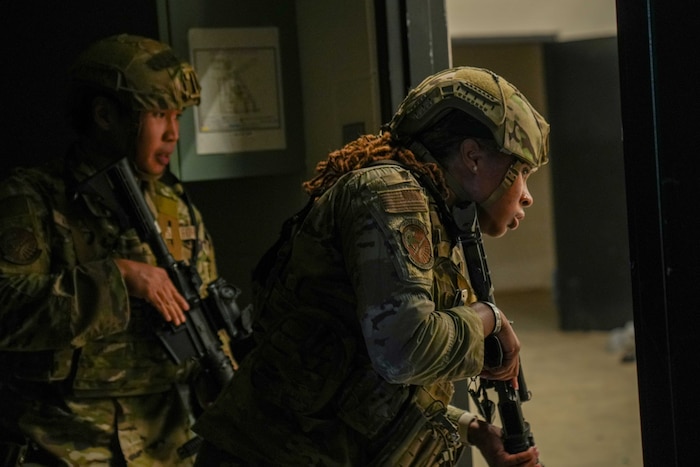 Two Airmen look through a doorway while holding weapons