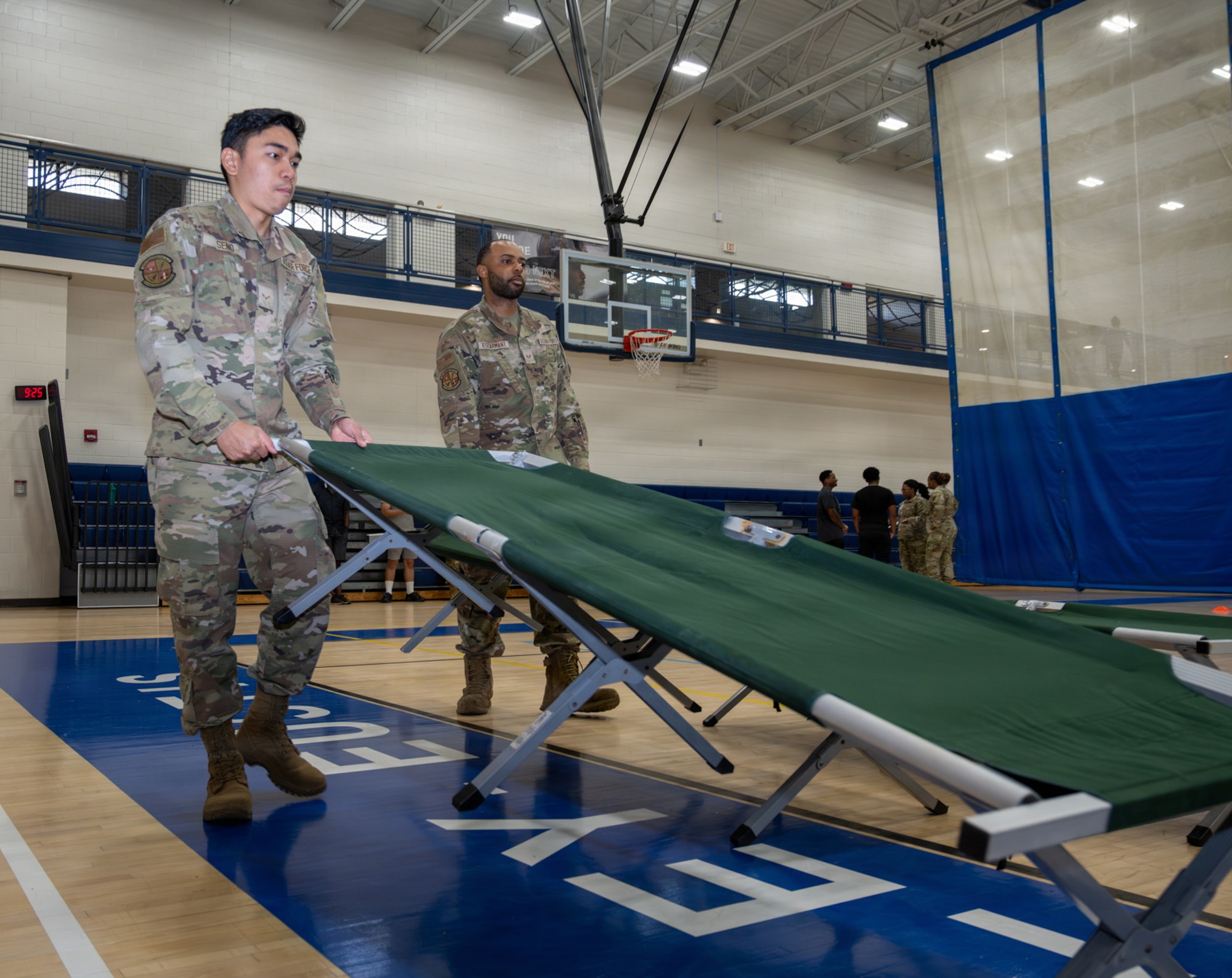 Two Airmen lift a cot.