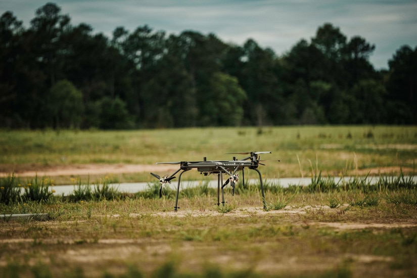 A military drone sits in a grassy field.