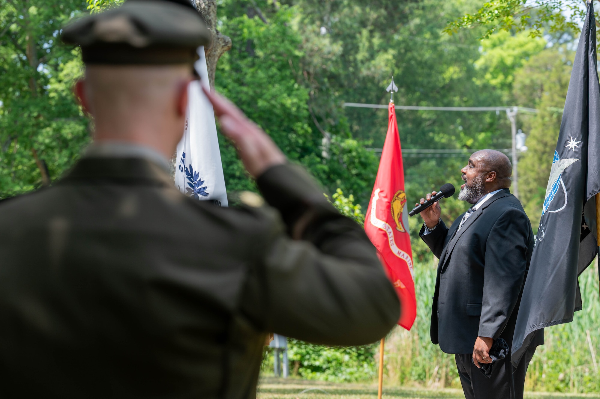 Photo of the back of a solider on the left and a civilian on the right singing into a microphone.