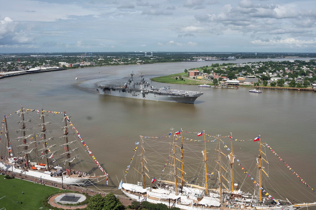 A ship transits a body of water on the shoreline under a blue sky.
