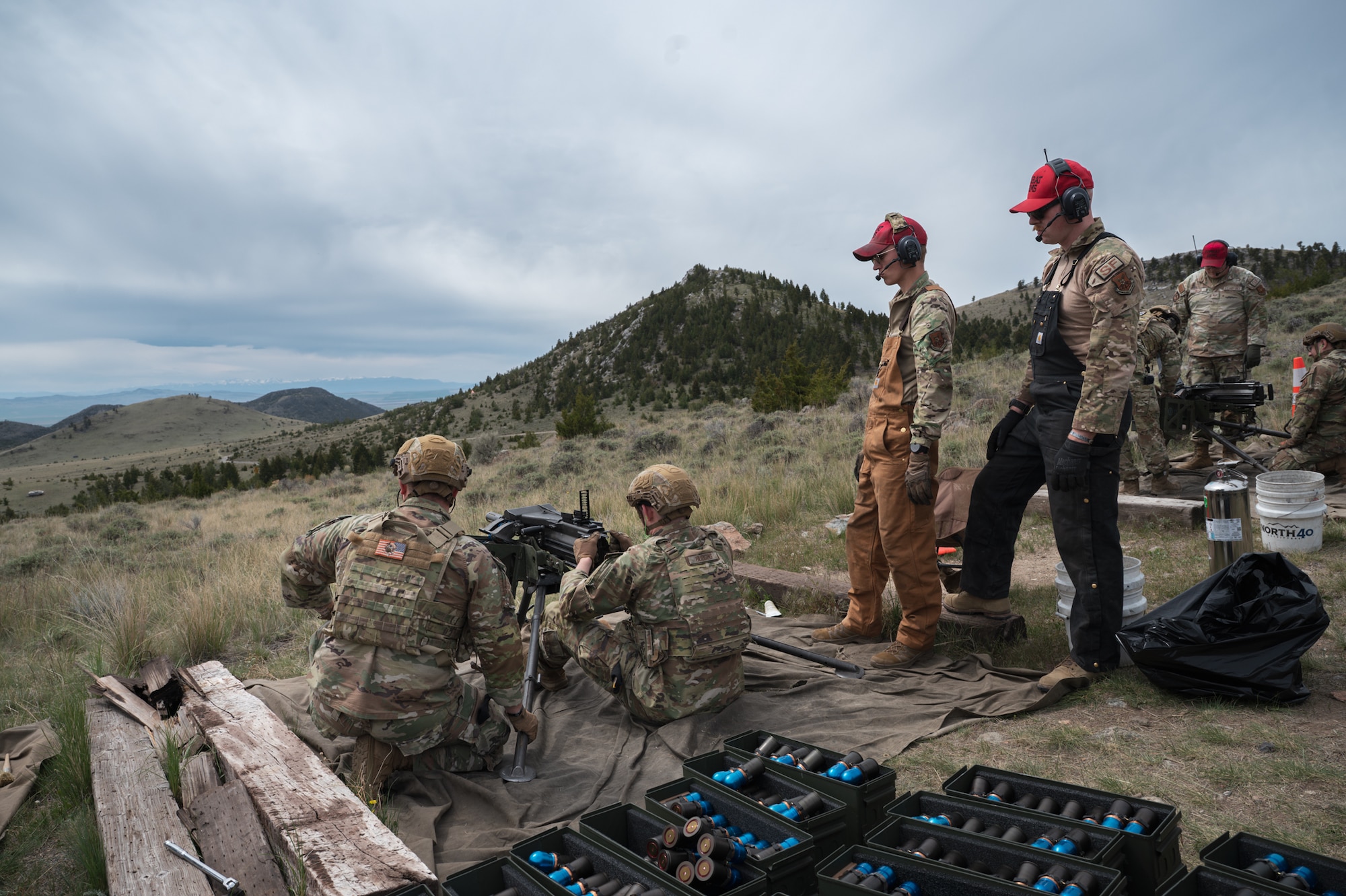 Two uniformed service members instruct two additional personnel during live-fire training with an Mk 19 grenade launcher.