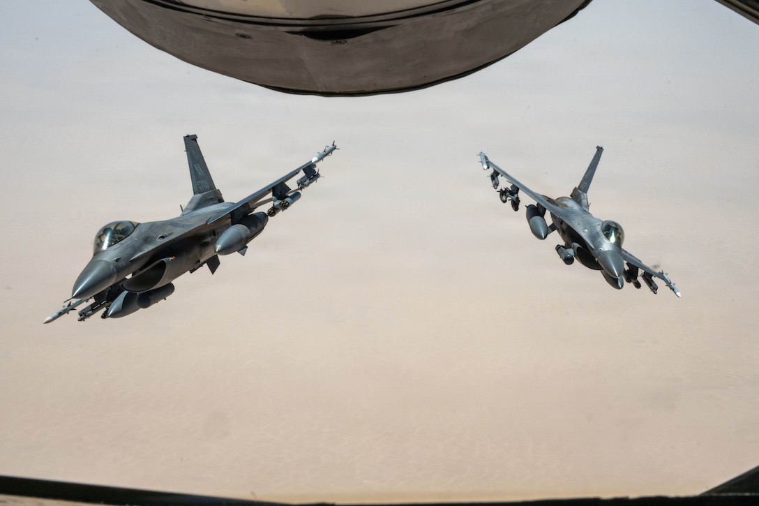 Two fighter jets fly near each other, and part of another aircraft is seen above them.