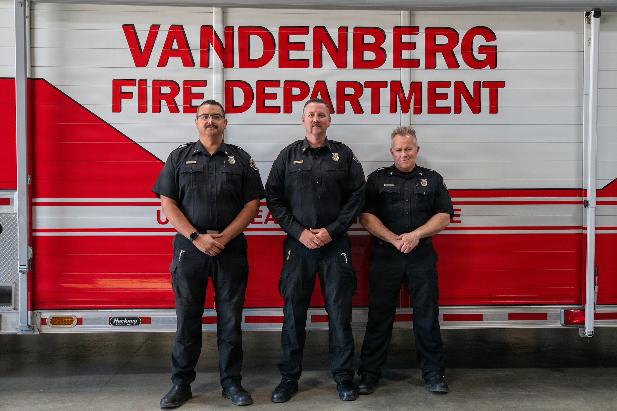 Three people stand together posed for a group photo in front of a firetruck.