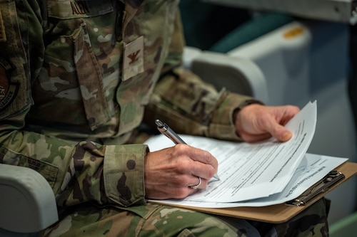 A close-up of a military member's hands as they use a pen to annotate notes on a paper form