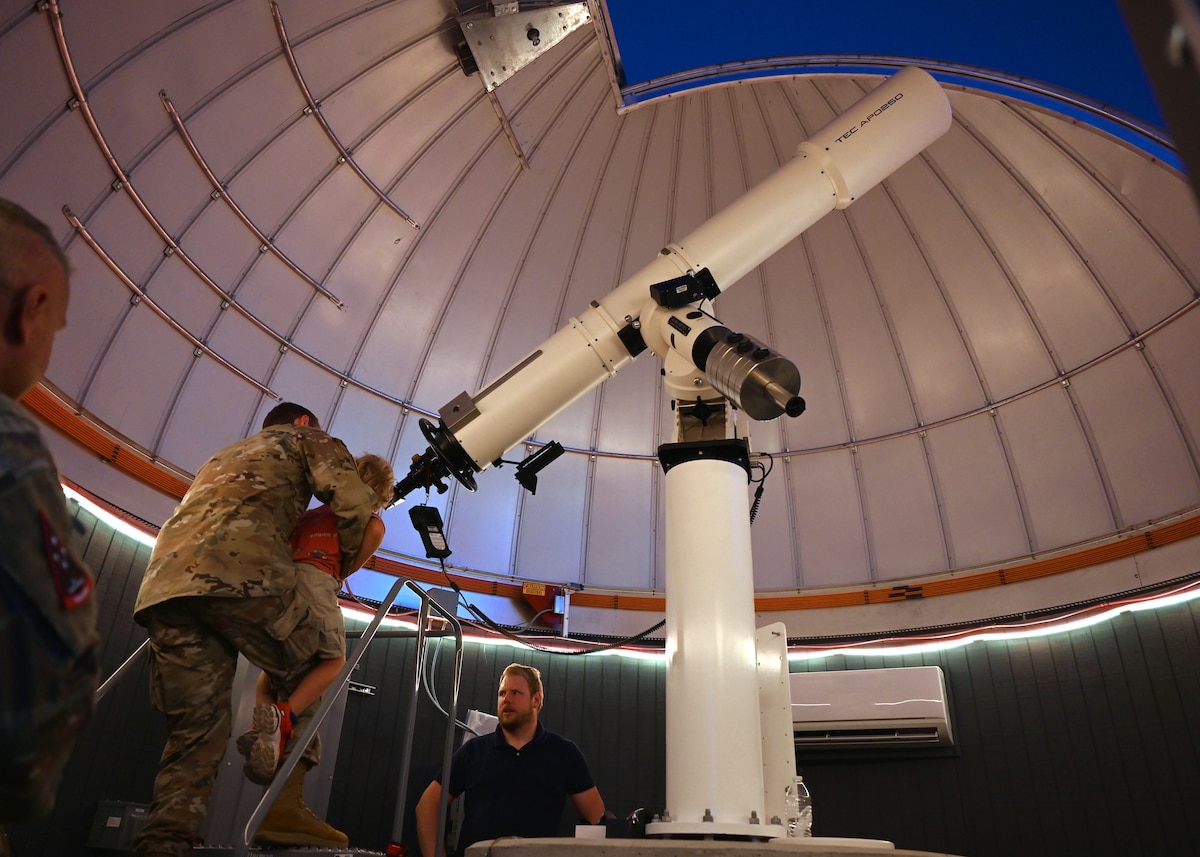 U.S. Space Force Capt. Justin Lee, Space Systems Command liaison to Space Forces Southern and U.S. Southern Command, lifts his child to look through a telescope during a space immersion tour at the Space4 Center in Oracle, Arizona, May 27, 2026. The hands-on experience provided attendees with a firsthand look at how telescopes and observational technologies are used to identify, track and characterize objects in space. (U.S. Air Force photo by Staff Sgt. Abbey Rieves)