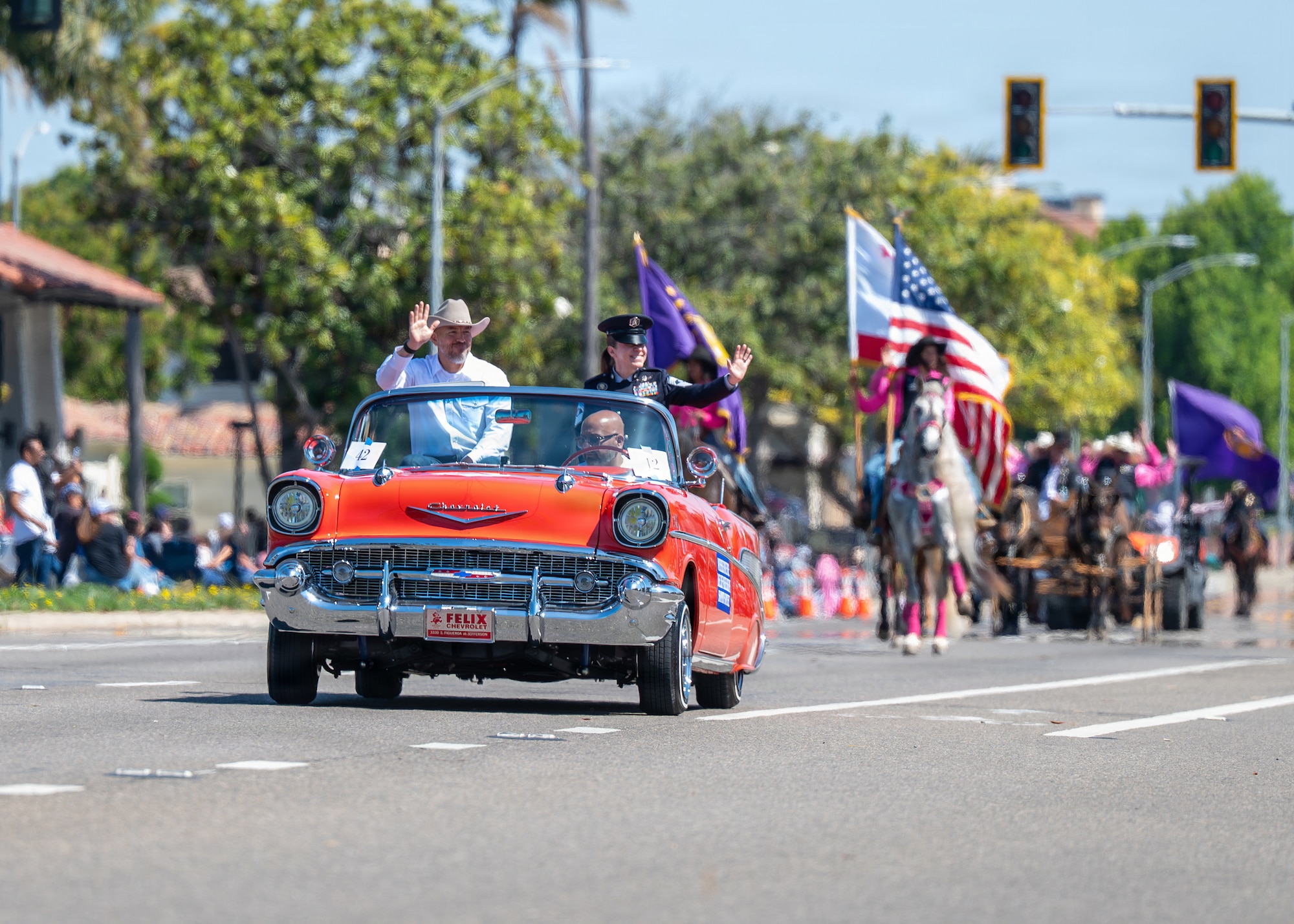 Orange car drives down the street followed by horses with flags.