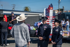 Two military troops talk with a man in cowboy hat.