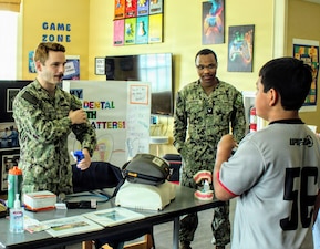 Hospital Corpsman 2nd Class Daniel Strunk, assigned to Navy Medicine Readiness and Training Command (NMRTC) Patuxent River, demonstrates the use of a tourniquet to a local student during the Share Fair at the Naval Air Station Patuxent River Youth Center. Coordinated by NAS Patuxent River School Liaison Officer Dawn Simpson, the event allowed homeschooling families to connect and learn about base resources, with NMRTC Pax River personnel providing interactive medical readiness demonstrations and conversations with families.
