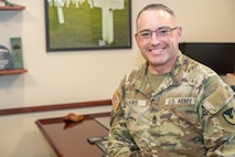 A person wearing a military uniform poses for a photo in an office.